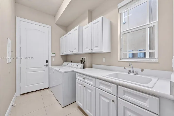 Laundry area featuring white cabinetry, a built-in drop-in sink, solid-surface countertops, and tile flooring