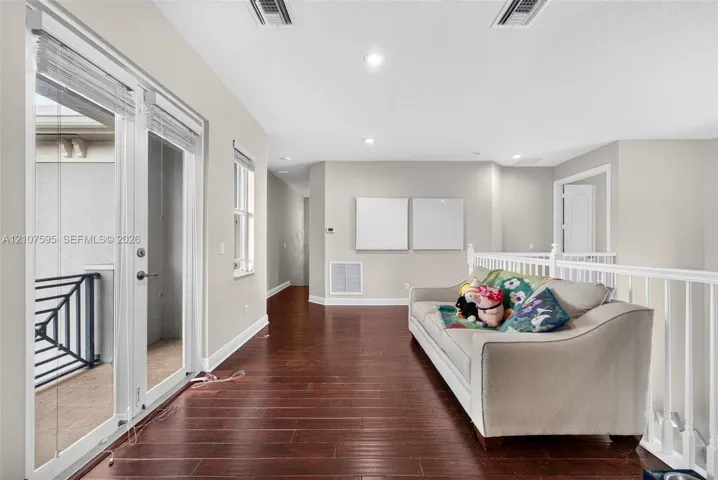 Wood-finish flooring, recessed lighting, double glass-panel doors, and a white balustrade railing