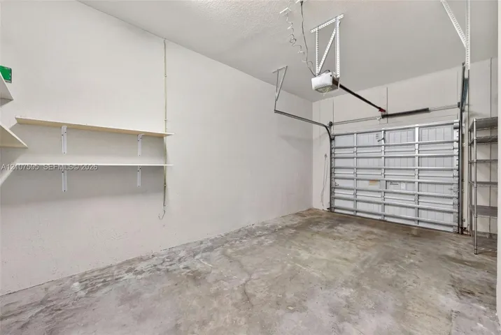Attached garage featuring concrete flooring, a paneled overhead door, an automated ceiling-mounted door opener, and fixed wall-mounted shelving