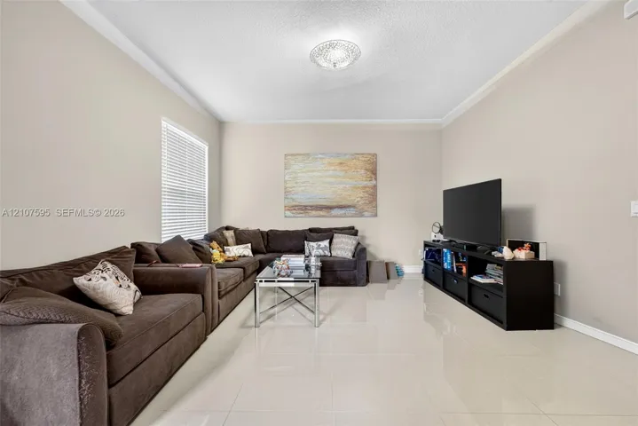 Spacious room featuring neutral wall tones, large-format tile flooring, crown molding, and a central ceiling-mounted light fixture