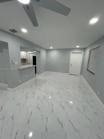 Polished tile flooring with high-contrast veining, recessed lighting, ceiling fan, and a pass-through breakfast bar featuring stone-surface countertop