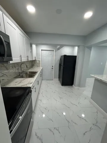Kitchen featuring white shaker-style cabinetry, stone-patterned countertops, large-format tiled flooring, recessed lighting, and integrated stainless steel microwave