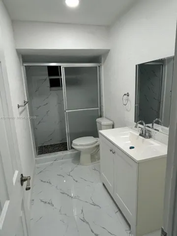 Bathroom featuring white cabinetry with integrated countertop, polished large-format tile flooring, shower enclosure with glass doors, and decorative wall tiling