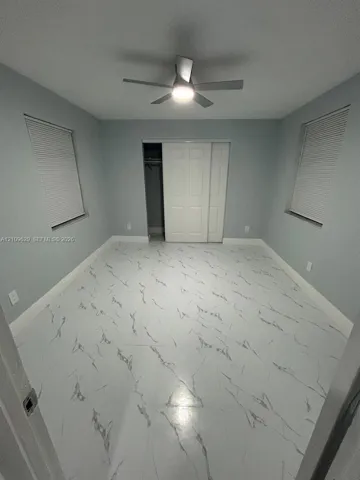 Interior space featuring light-toned, high-contrast patterned flooring, dual windows with integrated blinds, a ceiling fan with integrated lighting, and a closet with sliding paneled doors