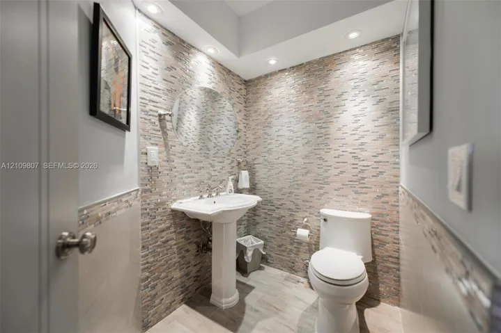 Powder room featuring a stacked-stone accent wall, pedestal sink, recessed lighting, and wood-finish tile flooring