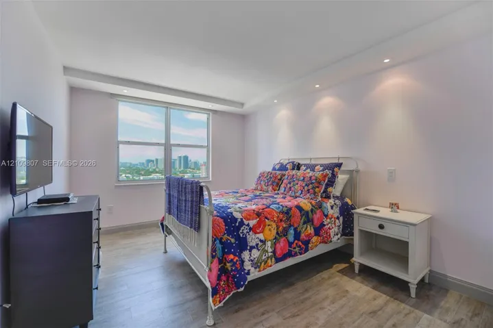 Room featuring wood-finish flooring, recessed ceiling lighting, and a large window with urban scenery