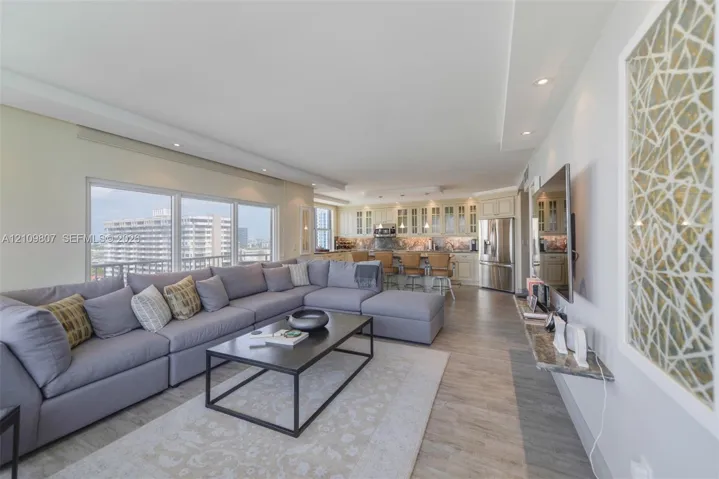 Open-concept main living area featuring wood-finish flooring, recessed lighting, floor-to-ceiling windows, built-in kitchen cabinetry, and a stone-topped wall-mounted shelf