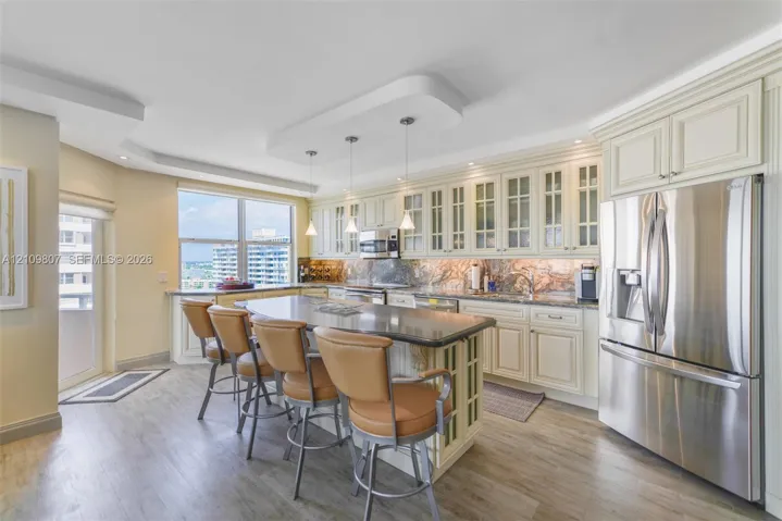Kitchen featuring cream cabinetry with glass-panel upper doors, a central island with a stone countertop, stainless steel refrigerator, and recessed lighting