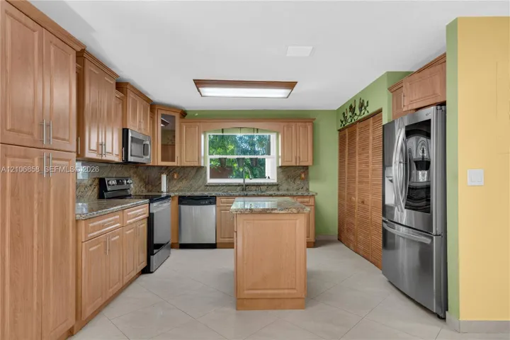 Kitchen featuring wood cabinetry, stone countertops, stainless steel appliances, a center island, and tile flooring
