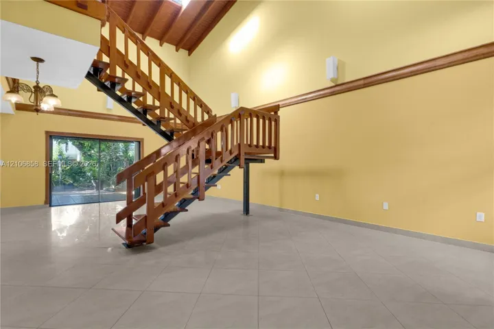 Vaulted ceiling with exposed wood-beam detailing, open-tread staircase with wood railings, large-format tile flooring, and oversized sliding glass doors