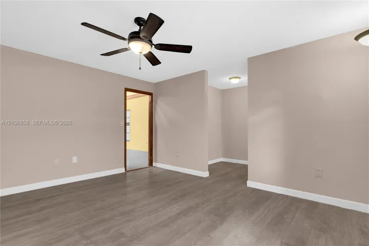 Interior space featuring neutral-toned walls, wood-finish flooring, a five-blade ceiling fan with integrated lighting, and multiple flush-mount ceiling light fixtures