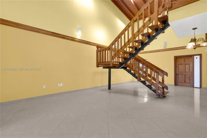 Vaulted ceilings with exposed timber beams, open-concept staircase with wood railings and steel framing, ceramic tile flooring, and custom wood-paneled entry door
