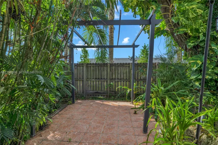 Outdoor patio area featuring a stone-tile floor, a dark-finished metal pergola, and perimeter wood fencing surrounded by dense mature vegetation