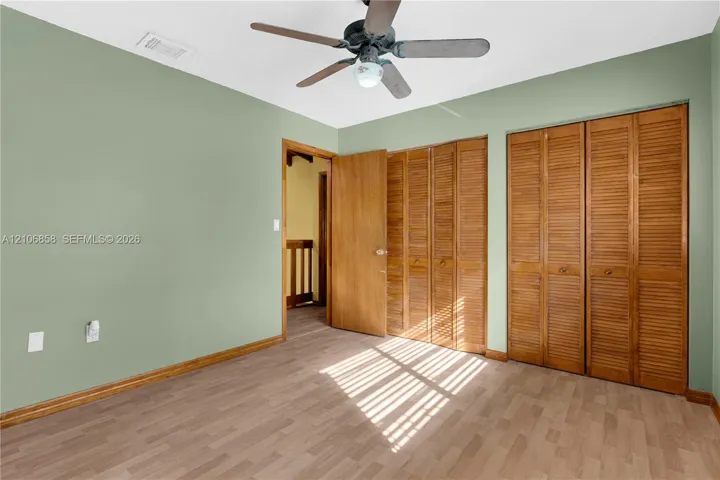 Room featuring wood-finish flooring, dual bi-fold louvered closet doors, and a ceiling fan