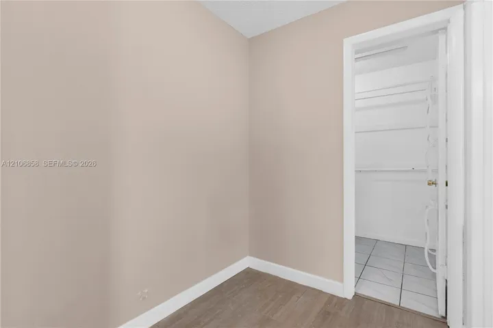 Neutral-toned interior featuring wood-finish flooring, white door casing, and a reach-in storage area with built-in shelving and light-colored tile flooring