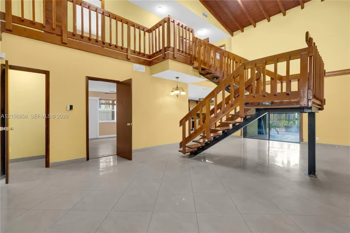Vaulted ceilings with exposed wooden beams, tile flooring, and a multi-level wooden staircase with balustrade railings