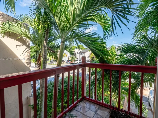 Elevated balcony featuring a red-painted wood balustrade and tiled flooring, framed by mature palm trees