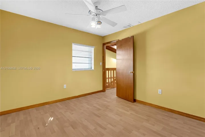Room featuring wood-finish flooring, a white ceiling fan with integrated lighting, and a window with horizontal blinds