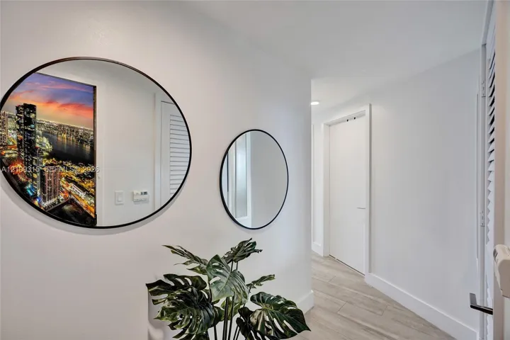 Hallway featuring wood-finish flooring, two circular wall-mounted mirrors with thin black frames, and louvered-style closet doors
