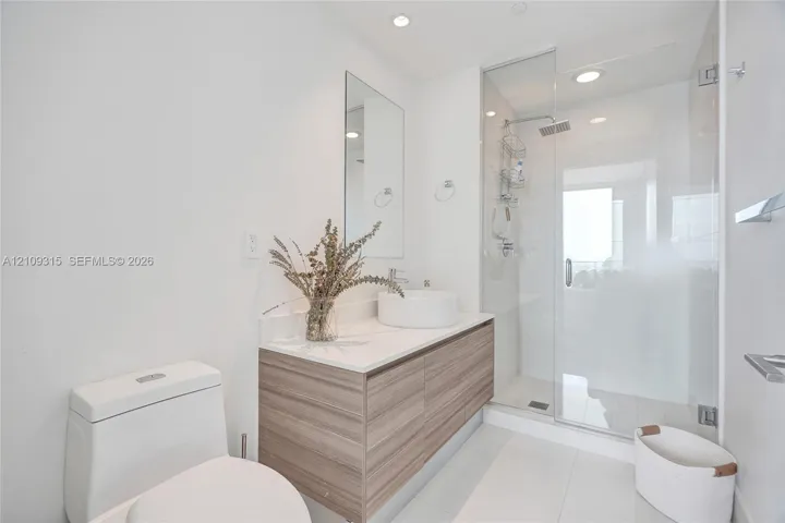 Floating wood-finish vanity with a white countertop and circular vessel sink, paired with a glass-enclosed walk-in shower featuring a rainfall showerhead
