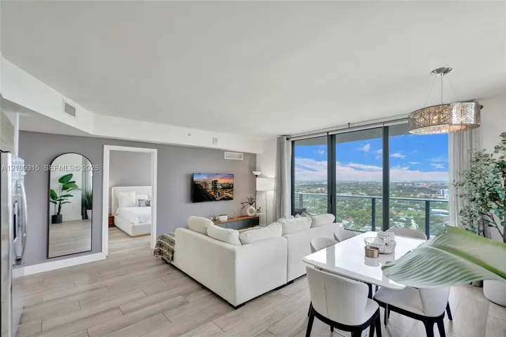 Open-concept living space featuring floor-to-ceiling windows, wood-finish flooring, a drum pendant light fixture, and an expansive balcony