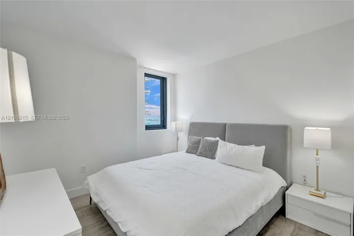 Neutral-toned room featuring wood-finish flooring, a tall vertical window, and crisp white wall finishes