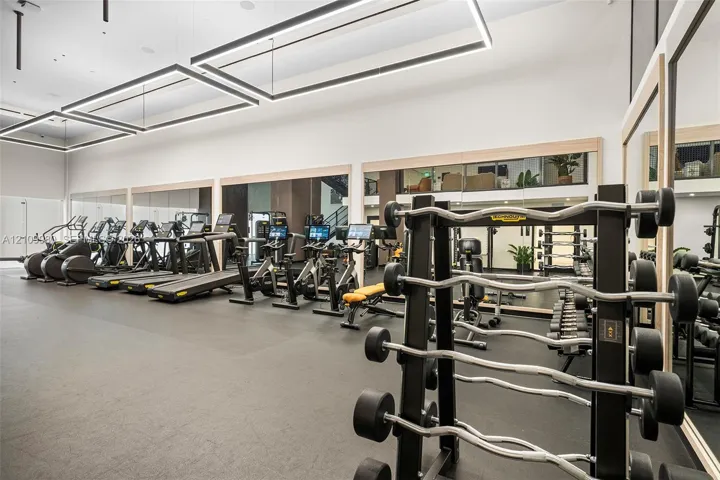 Fitness facility featuring high ceilings, rectangular modern pendant lighting, expansive wall-to-wall mirrors, and durable flooring