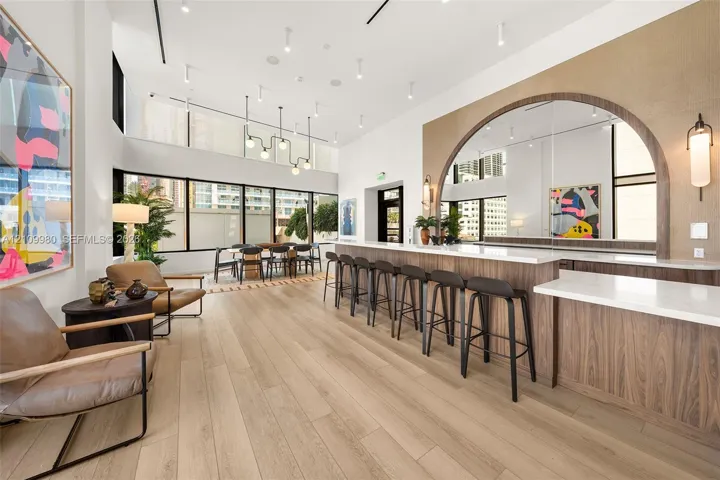 High-ceiling interior featuring wood-finish flooring, a large bar with a stone-surface countertop, an arched mirror display, and expansive floor-to-ceiling windows