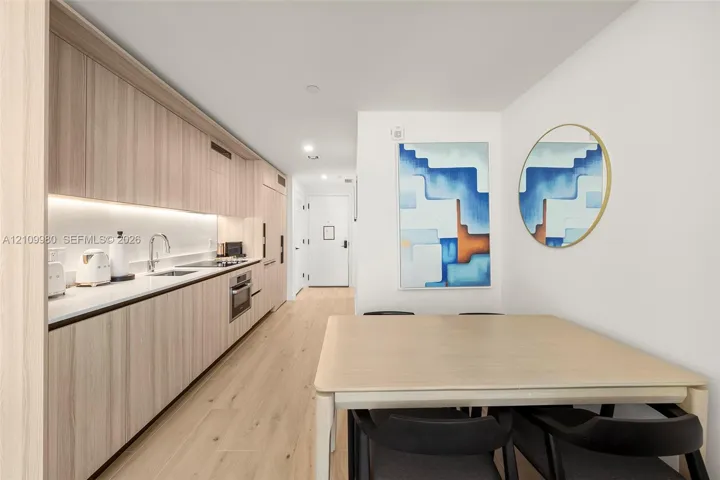 Kitchen featuring light wood-finish cabinetry, solid surface countertops, integrated appliances, under-cabinet lighting, and wood-finish flooring
