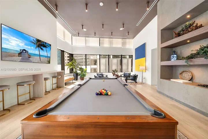 High-ceilinged room featuring wood-finish flooring, recessed ceiling lighting, a built-in stone-finish wall niche with integrated shelving, and a continuous built-in wall shelf