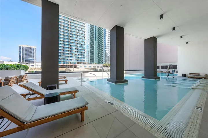 Covered swimming pool featuring large structural columns, light-toned tile decking, and recessed ceiling lighting