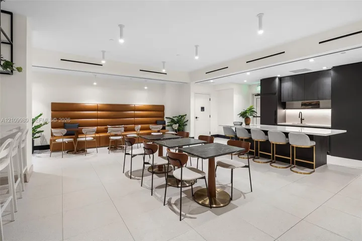 Large common room featuring tile flooring, recessed ceiling lighting, a built-in upholstered wall bench, and a kitchenette with quartz countertops and dark cabinetry