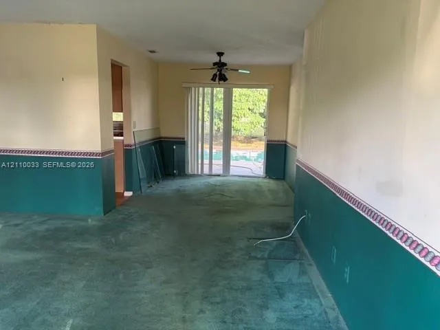 Carpeted flooring, dual-tone wall treatment with decorative border, ceiling-mounted fan with light fixture, and sliding glass doors