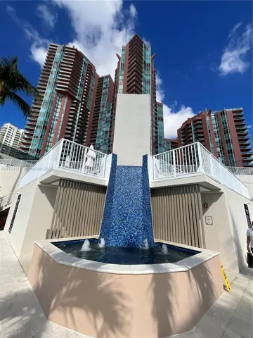 Cascading water feature with blue mosaic tiling, multi-story high-rise architecture, white metal railings, and concrete hardscaping
