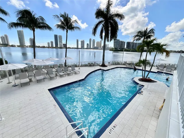 In-ground swimming pool with stone-tile decking, metal safety railing, and surrounding palm trees