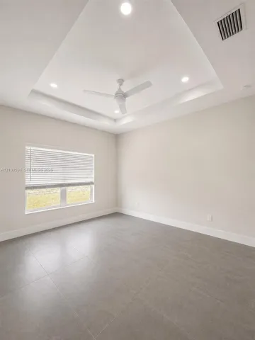 Tray ceiling featuring a central white ceiling fan, recessed lighting, and large-format tile flooring