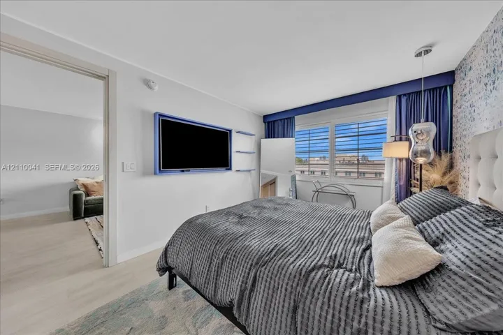 Bedroom featuring wood-finish flooring, multi-pane window, built-in television mount, decorative accent wall, and pendant lighting