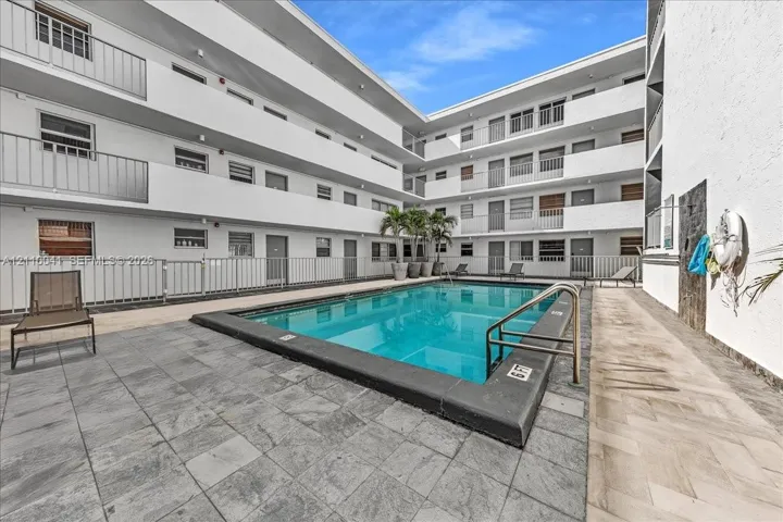 Outdoor swimming pool featuring a concrete deck, multi-level exterior balconies with metal railings, and natural stone-finish hardscaping