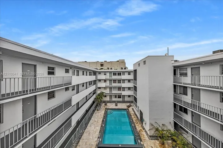 Rectangular swimming pool featuring a stone-paver deck and surrounding multi-story building exterior with metal balcony railings
