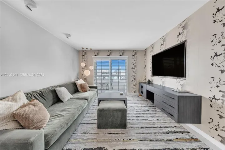 Floating charcoal-finish media console, patterned accent wallpaper, glass sliding doors with plantation shutters, and a trio of pendant lights
