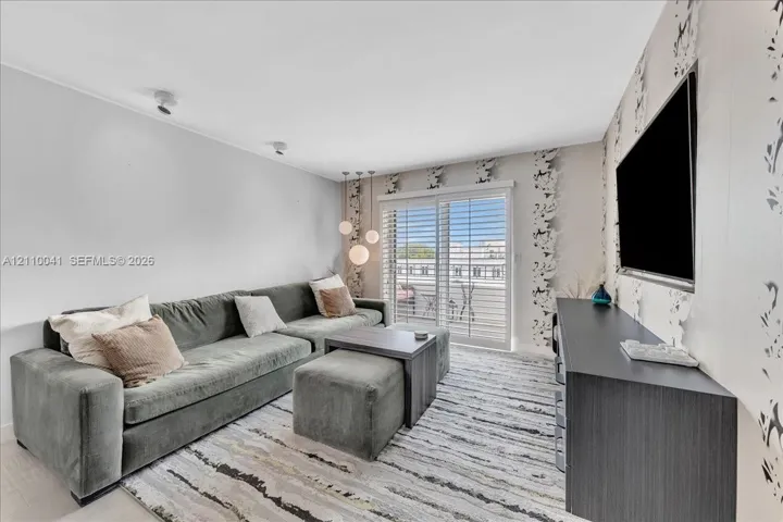 Living area featuring glass sliding doors with plantation shutters, recessed ceiling lighting, three-globe pendant lighting, and an accent wall with patterned wall covering