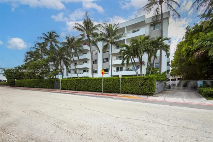 Multi-story building featuring private balconies, a gated entrance, and landscaped perimeter hedging