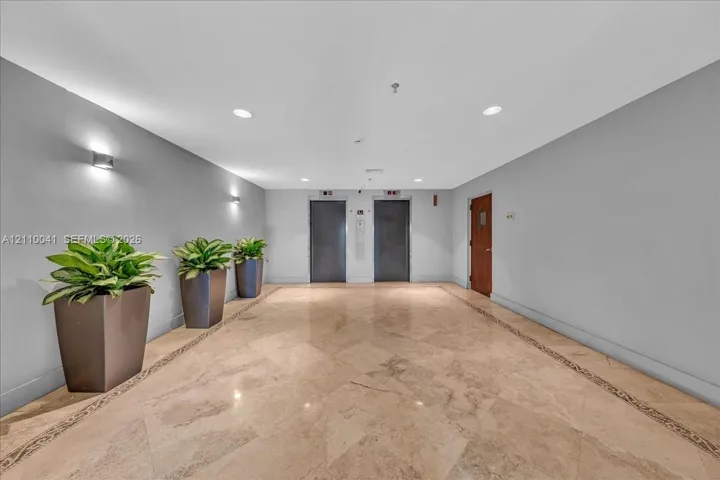 Common area lobby featuring polished stone flooring with decorative inlay, dual elevator banks, and recessed ceiling lighting
