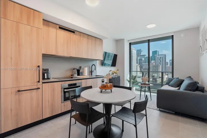 Kitchen featuring custom light-toned cabinetry, built-in panel-ready appliances, quartz countertops, and floor-to-ceiling glass sliding doors with an urban skyline backdrop