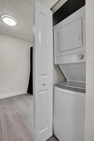 Stackable laundry unit housed within a closet featuring a white bi-fold door, recessed ceiling lighting, and wood-finish flooring