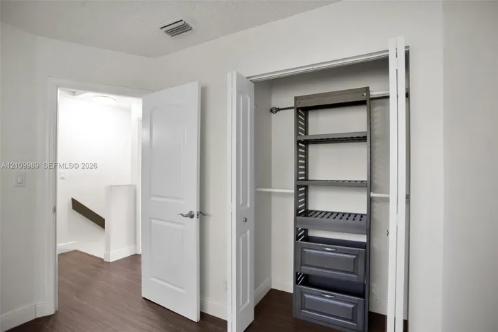 Closet featuring a built-in dark-finish organizer system with open shelving and dual drawers, complemented by wood-finish flooring and a white multi-panel interior door