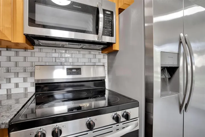 Kitchen featuring stainless steel appliances, glass-tiled backsplash, natural-finish cabinetry, and stone-surface countertops