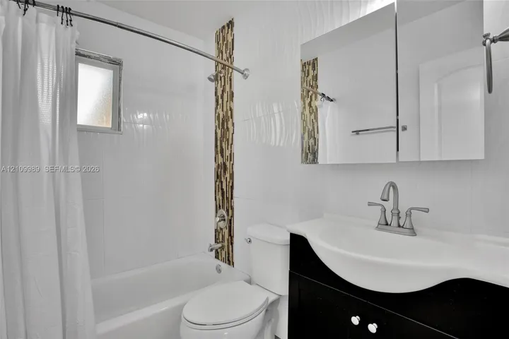 Bathroom featuring white textured wall tile, a vertical stone-mosaic accent band, a black vanity with a molded basin, and a mirrored medicine cabinet