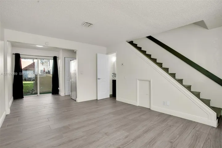 Open interior space featuring wood-finish flooring, staircase with a handrail, sliding glass door, and recessed storage area