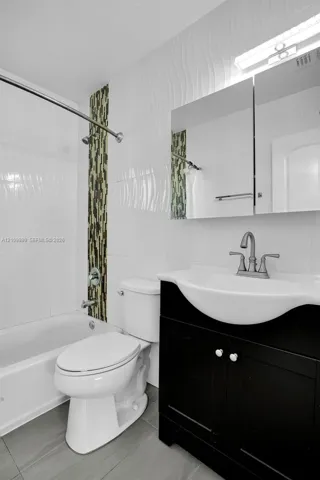 Bathroom featuring a dark wood-finish vanity, integrated sink, vertical mosaic tile accent, textured wall tile, and gray floor tiling